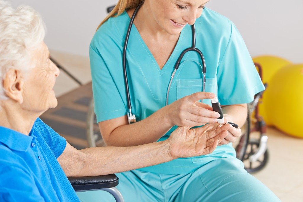 nurse monitoring blood sugar of old woman